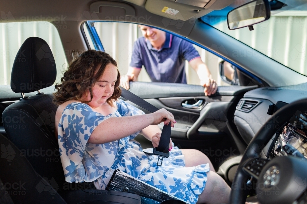 Young person with down syndrome putting on seatbelt in car - Australian Stock Image