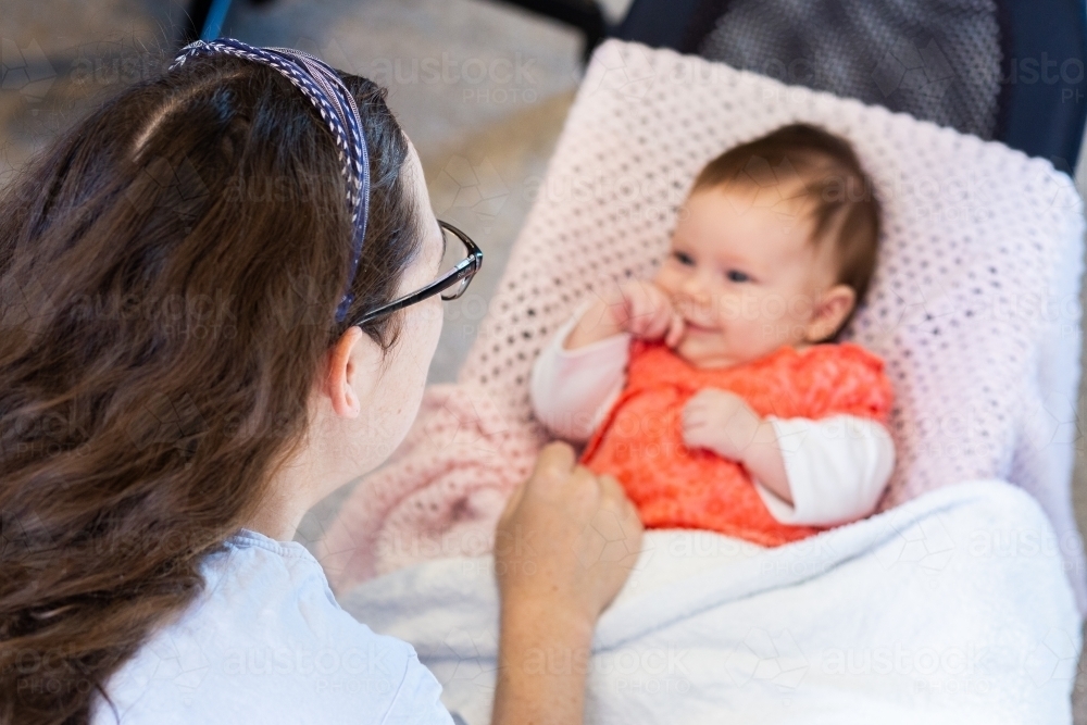 Young postpartum mother interacting with new-born baby in bouncer - Australian Stock Image