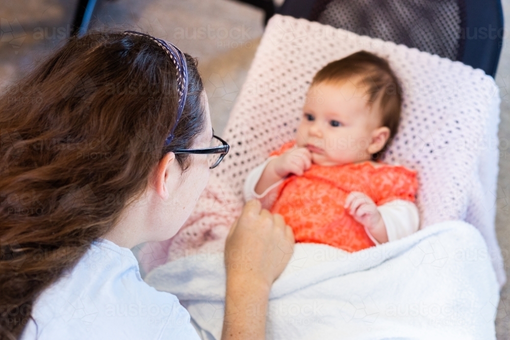 Young postpartum mother interacting with new-born baby in bouncer - Australian Stock Image