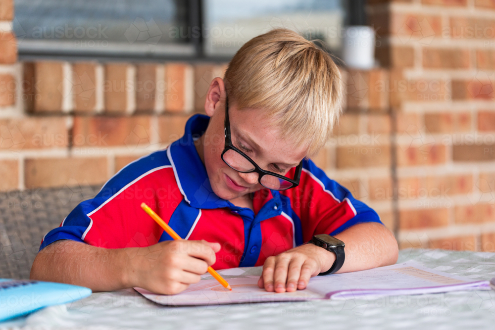 Image of Young primary school boy working on homework wearing glasses ...