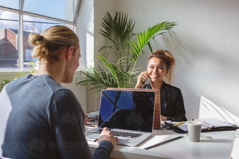 Young professional girl on the phone working opposite a colleague - Australian Stock Image