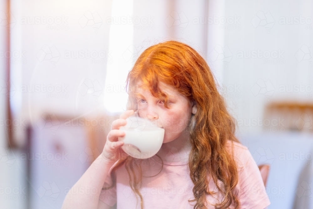 young red-haired girl drinking milk from a glass - Australian Stock Image