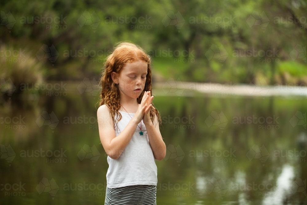 Young redhead girl looking at her hands by the riverside - Australian Stock Image