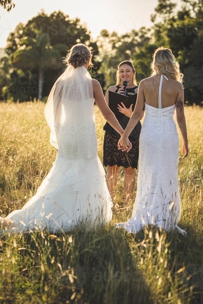 Young same sex brides holding hands getting married by celebrant - Australian Stock Image