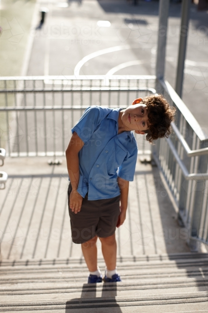 Young school boy at school tilting head on stairway - Australian Stock Image