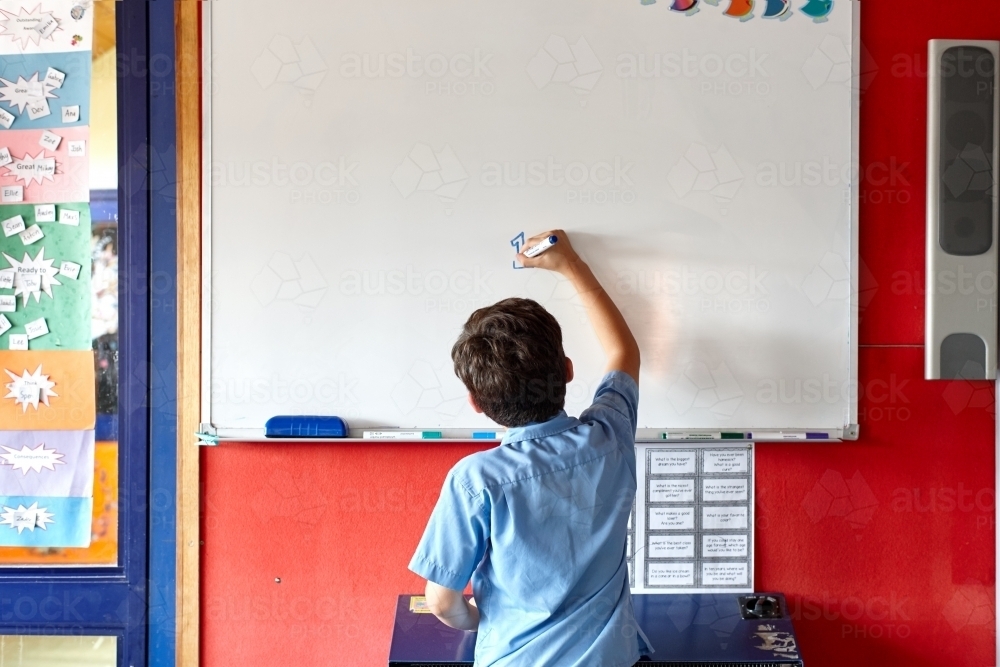 Young school boy at school writing on white board - Australian Stock Image