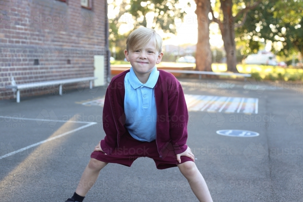 Young school boy bending down with hands on his knees - Australian Stock Image