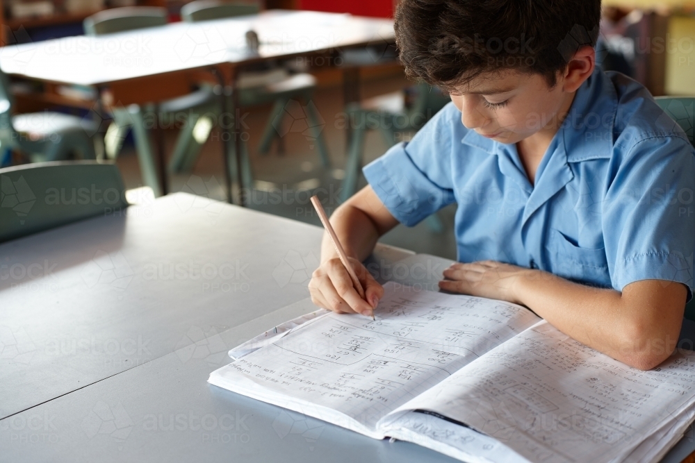 Image of Young school boy doing maths in class - Austockphoto