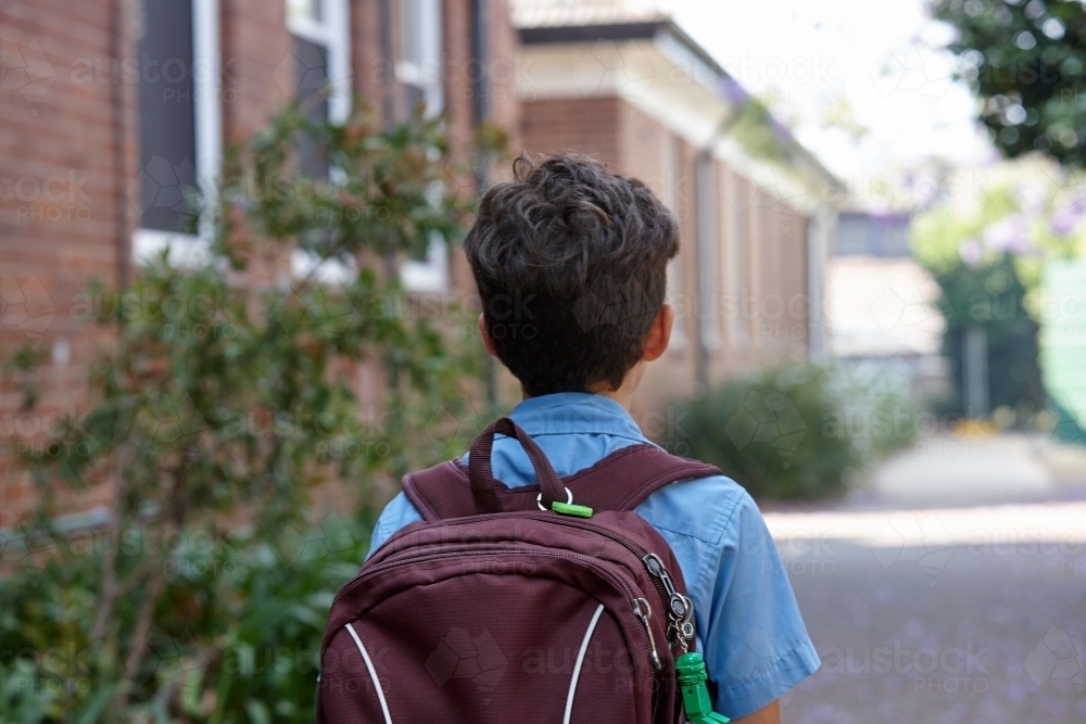Young school boy walking away from camera, to class - Australian Stock Image