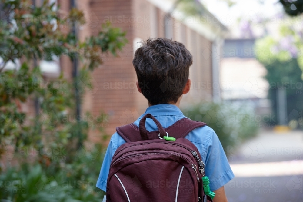 Young school boy walking away from camera, to class - Australian Stock Image
