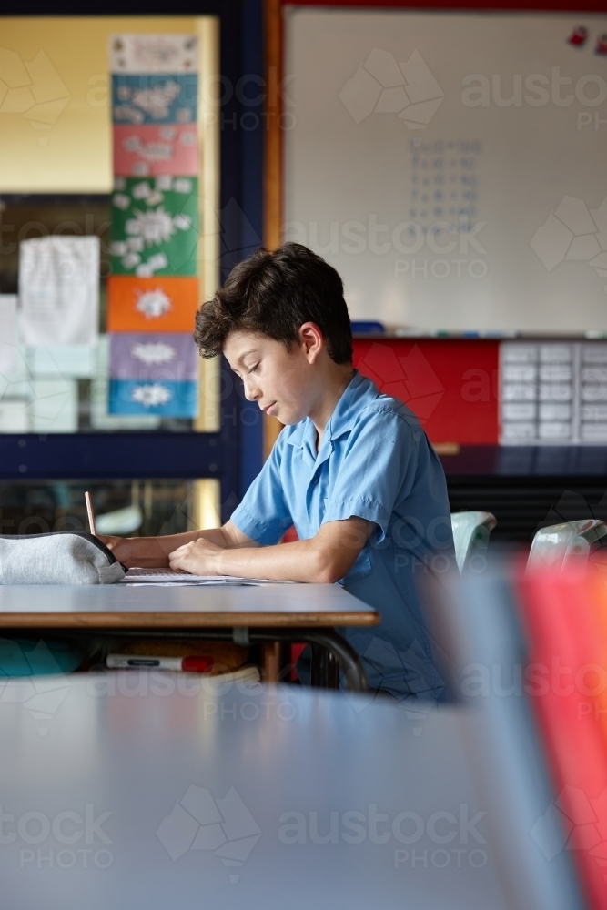 Young school boy working on homework in classroom - Australian Stock Image