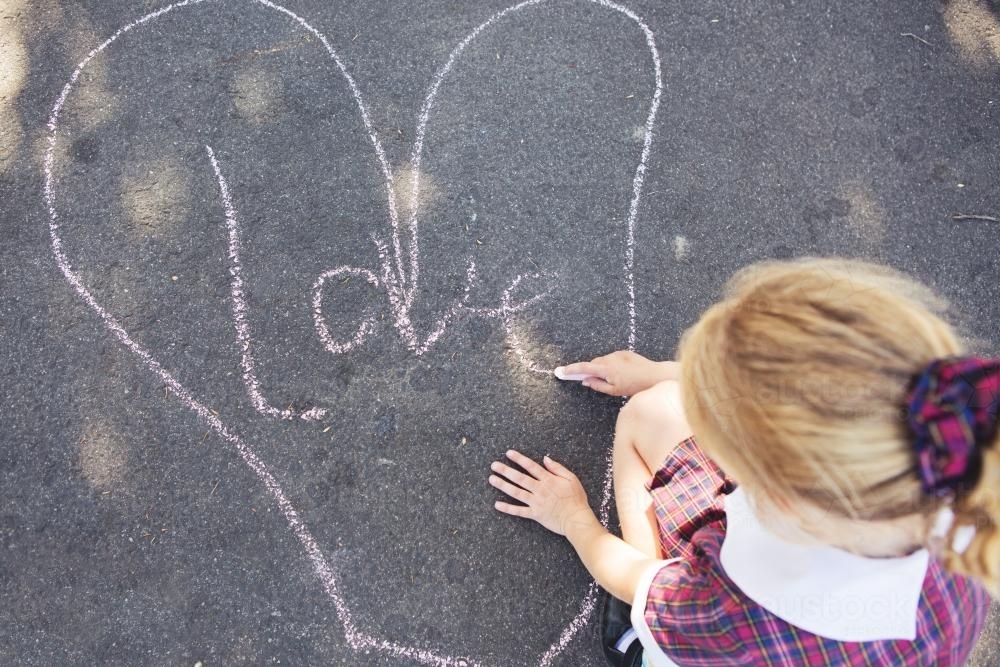 Young school girl drawing pictures on the road with chalk - Australian Stock Image