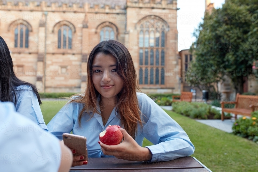 Young school girl eating apple whilst checking phone - Australian Stock Image