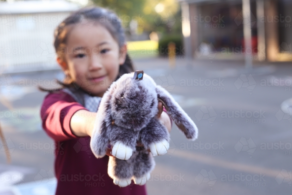 Young school girl holding out her toy bunny to the camera - Australian Stock Image