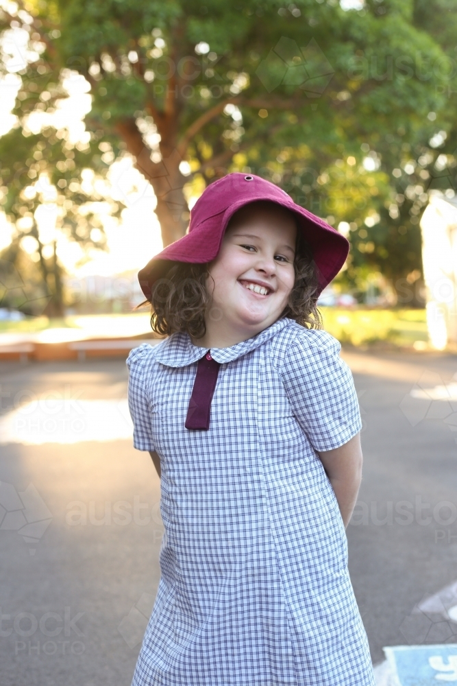 Image of Young school girl in uniform and wearing hat smiling outside ...