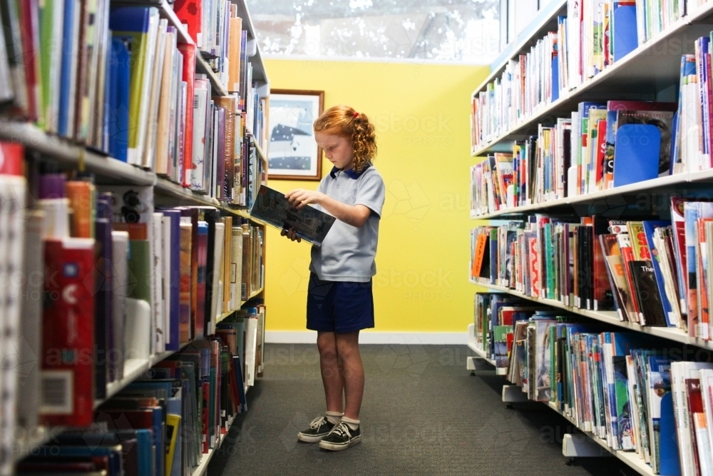 Young school girl looking at books in the Library - Australian Stock Image