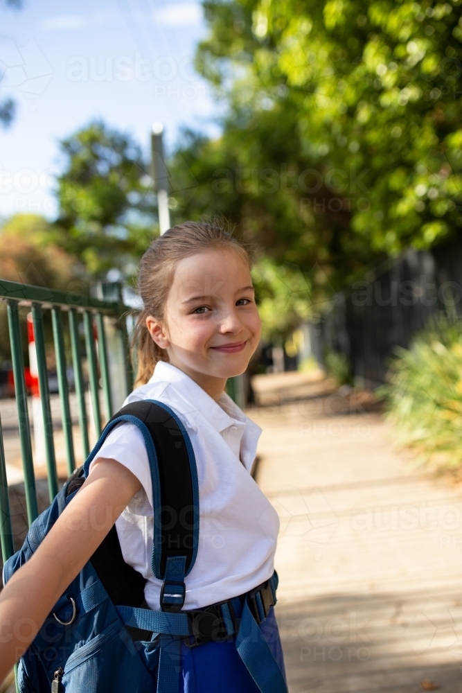 Young Schoolgirl Leaning Against Fence Smiling - Australian Stock Image