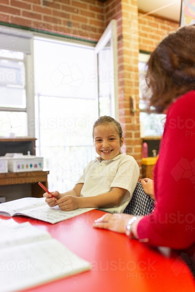 Image of Young schoolgirl sitting behind red desk in a classroom with ...