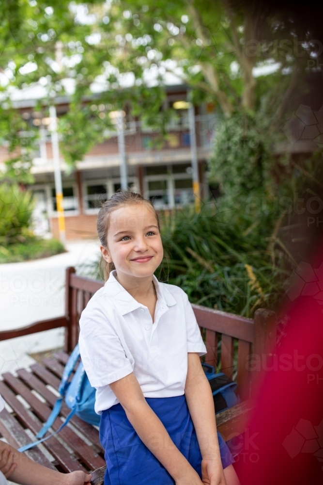 Image of Young Schoolgirl Sitting Outside Smiling - Austockphoto