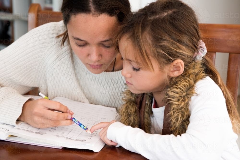 Young sister being taught by older sister while doing homework. - Australian Stock Image