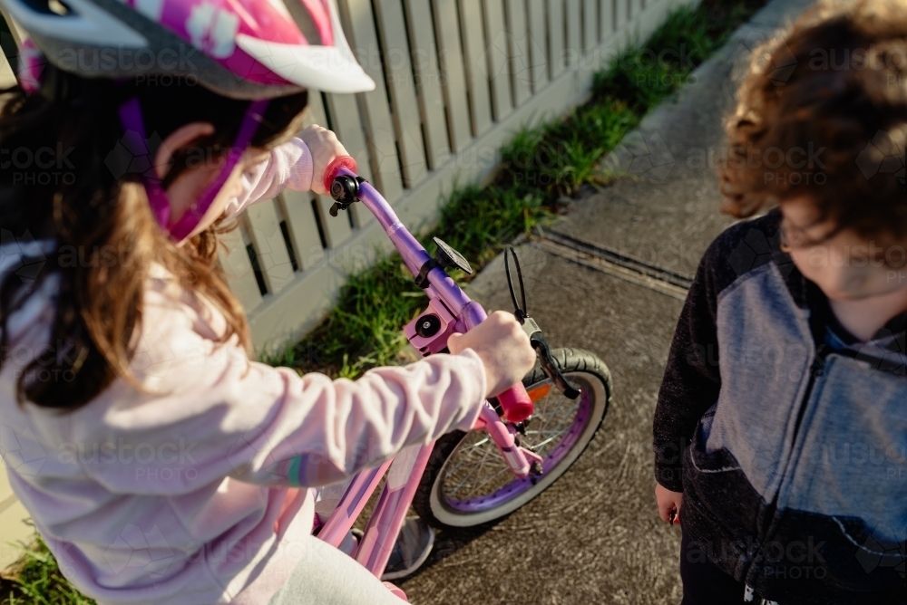 Young sister rides her bike on the footpath while her younger brother walks with her - Australian Stock Image