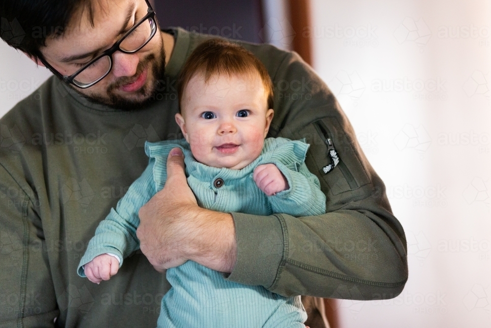 Young smiling baby held by father inside home - Australian Stock Image