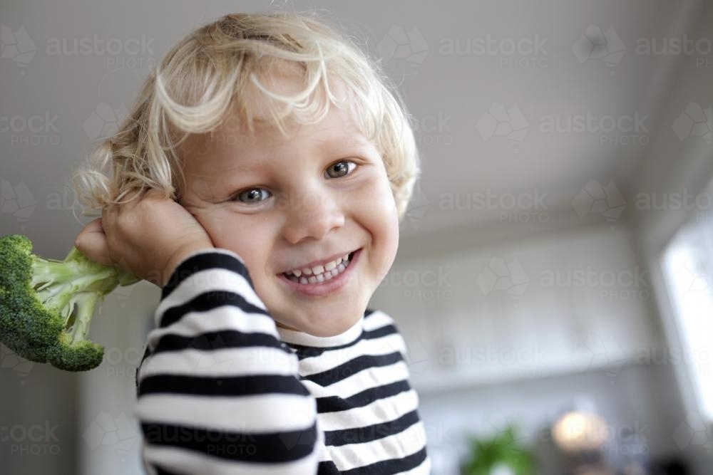 Young smiling boy holding broccoli up to ear - Australian Stock Image
