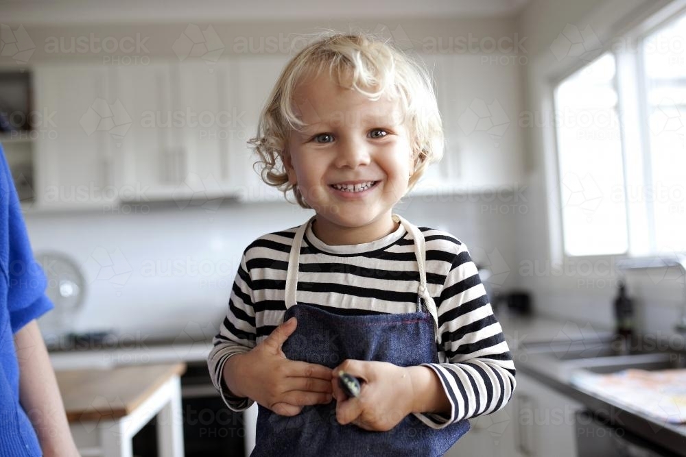 Young smiling boy wearing apron in kitchen - Australian Stock Image