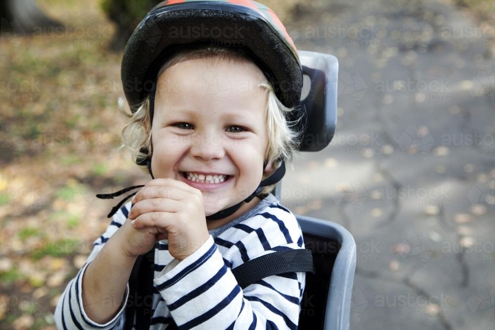 Young smiling boy with helmet in bike seat - Australian Stock Image
