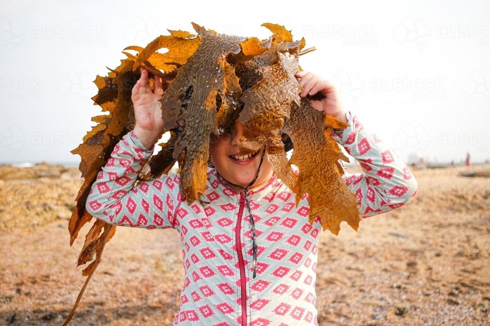 Young smiling girl holding a large piece of seaweed across her face - Australian Stock Image