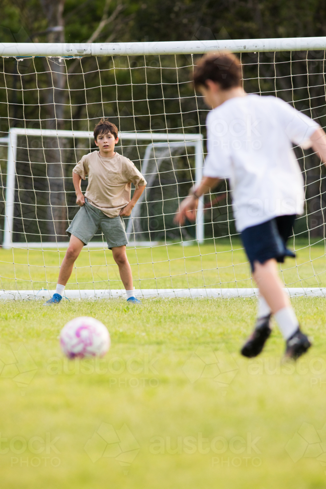Young soccer player on defensive stance in front of soccer goal net during penalty kick - Australian Stock Image