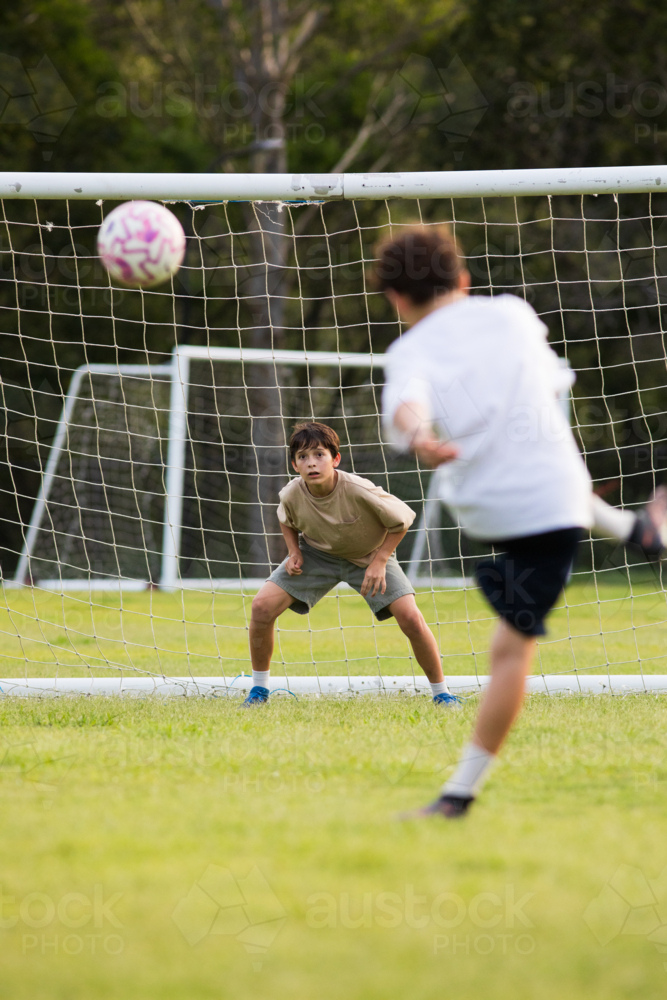 Young soccer player on defensive stance in front of soccer goal net during penalty kick - Australian Stock Image