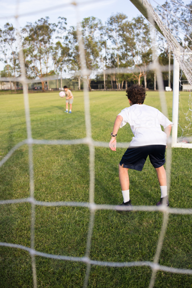 Young soccer player on defensive stance viewed through the soccer goal net during penalty kick - Australian Stock Image