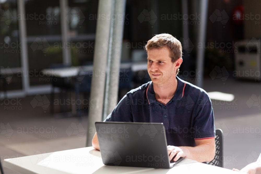 Young sole trader working on laptop in urban cafe setting - Australian Stock Image