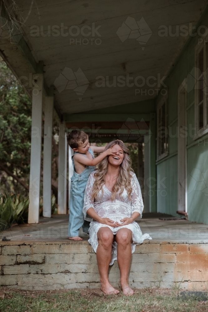 Young son covering his mother's eyes and playing with her on the front porch of home - Australian Stock Image