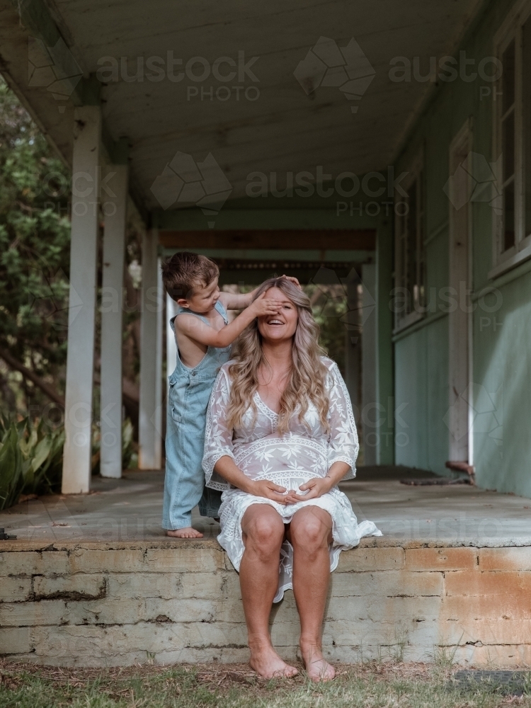 Young son covering his mother's eyes and playing with her on the front porch of home - Australian Stock Image
