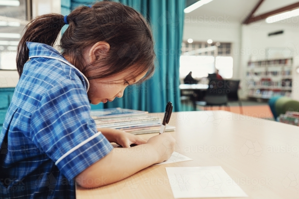 Young student girl writing in libary - Australian Stock Image