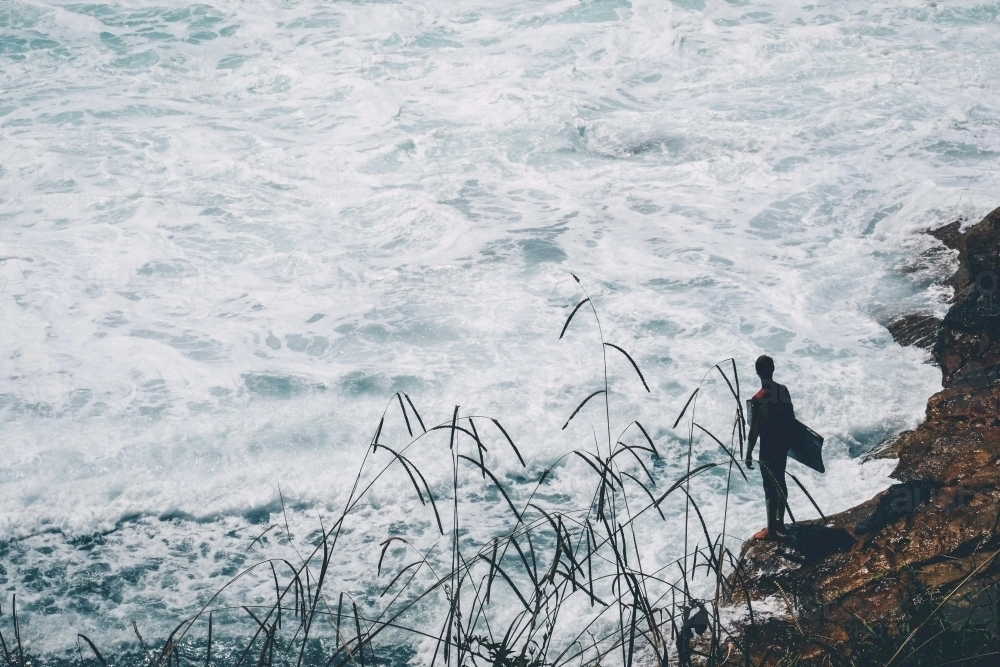 Young surfer standing on the rock next to the sea - Australian Stock Image