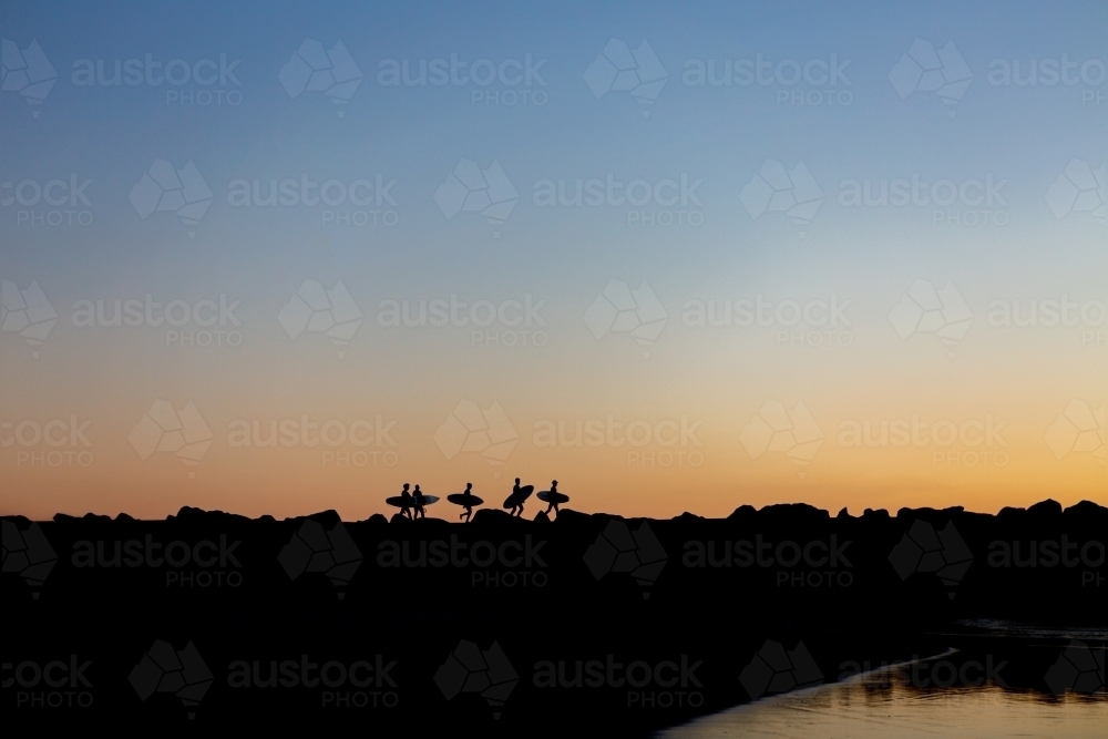 Young surfers walking the rock wall to the waves at dawn - Australian Stock Image