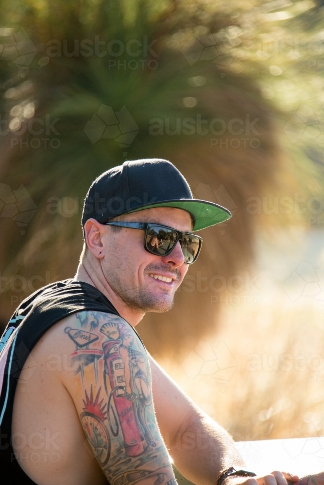 Young tattooed guy wearing sunnies and a cap - Australian Stock Image