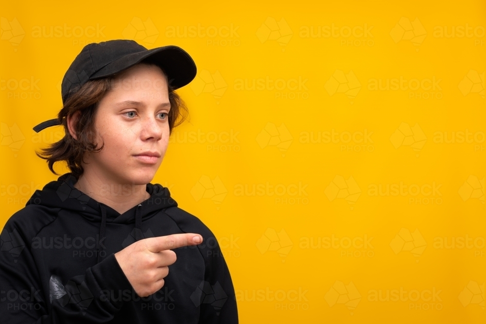young teen boy wearing black and pointing finger against yellow background - Australian Stock Image