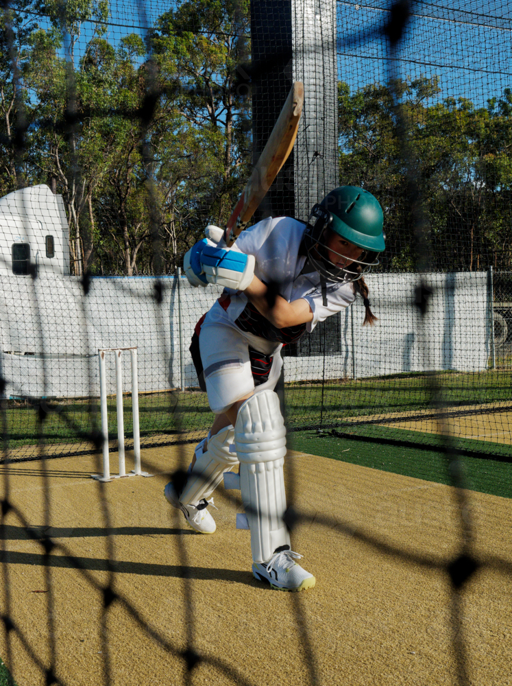 Young teen girl hitting shot during cricket net training - Australian Stock Image