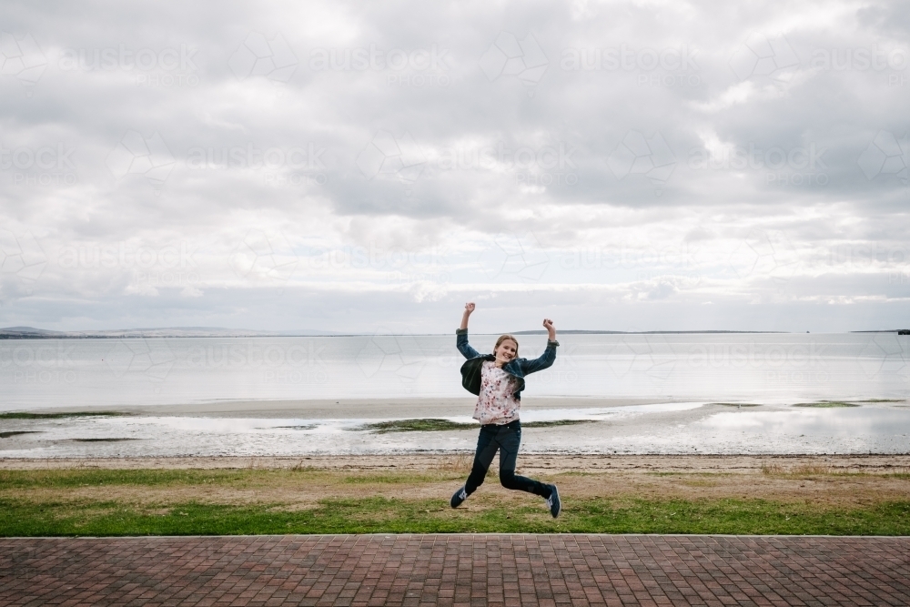 young teen girl jumping, ocean in the background - Australian Stock Image