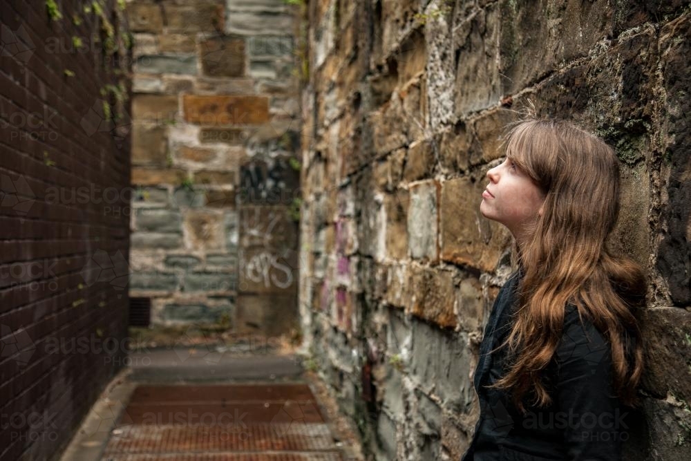 Young teen girl leaning on alleyway wall looking up - Australian Stock Image