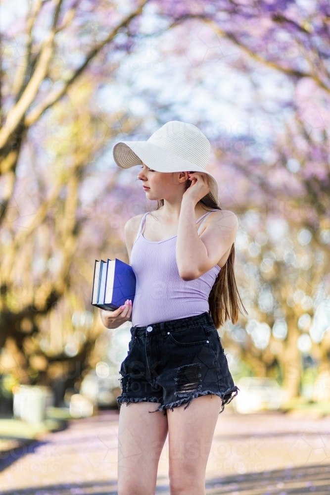 Young teen girl walking down street with hat and books under her arm - Australian Stock Image