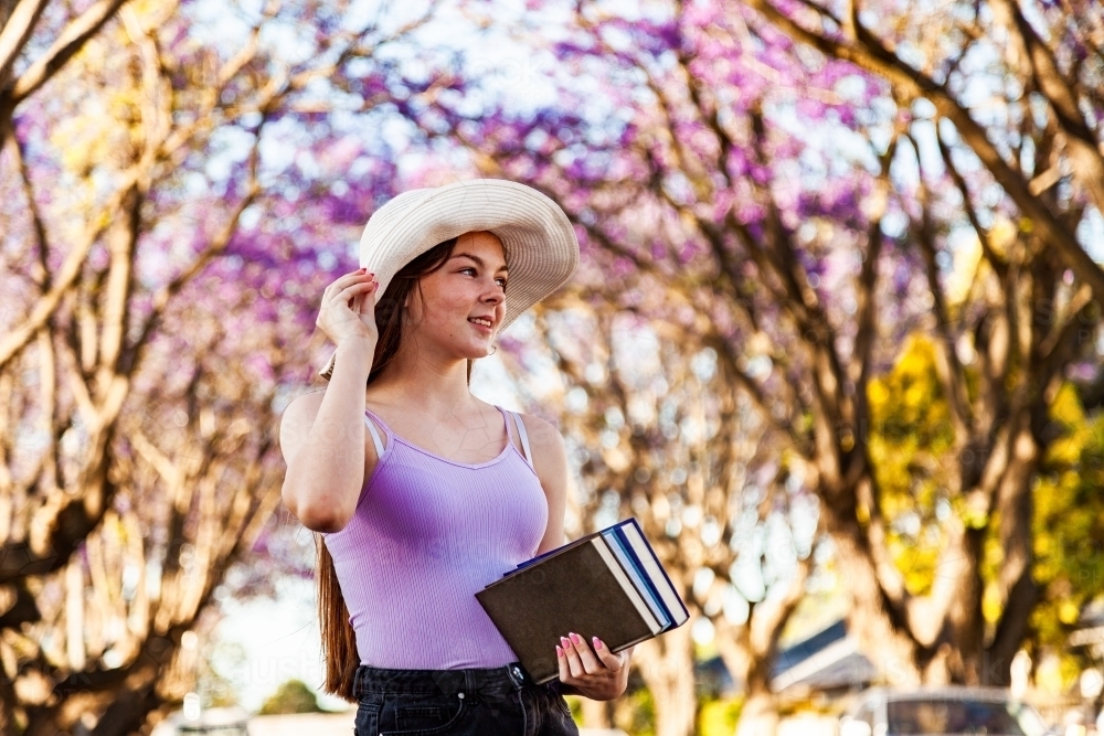 Young teen girl walking down street with hat and books under her arm - Australian Stock Image