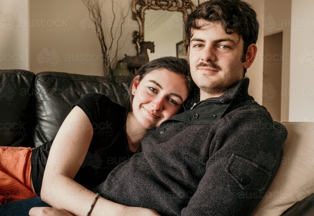 Young teenage couple cuddle on the couch. - Australian Stock Image