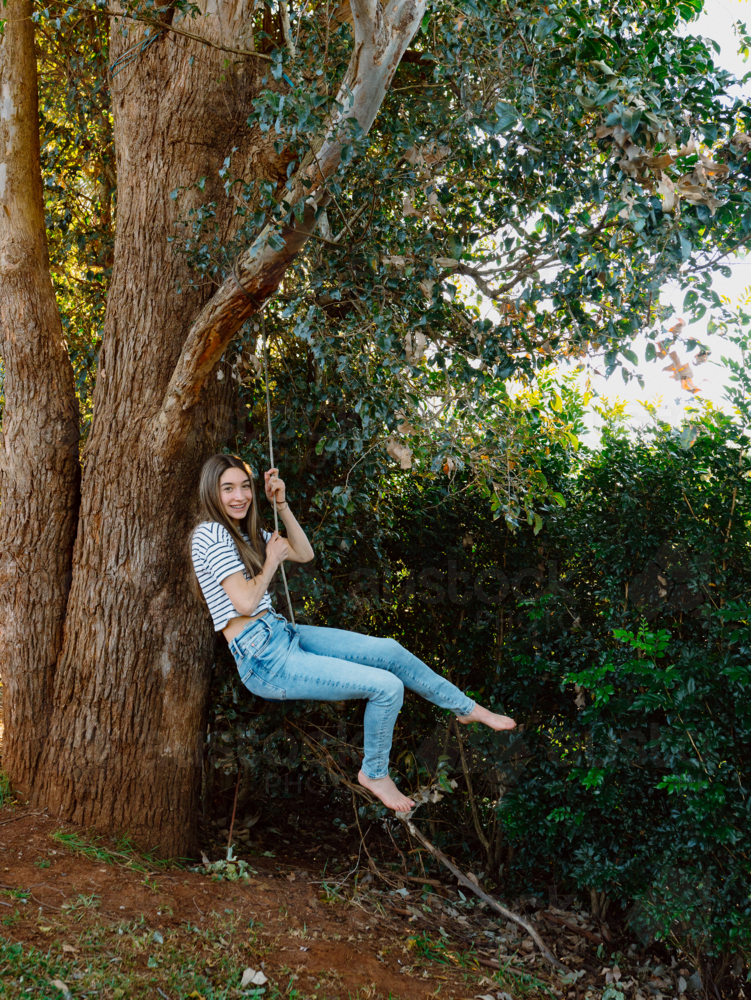 Young teenage girl hanging on a rope swing on the tree. - Australian Stock Image
