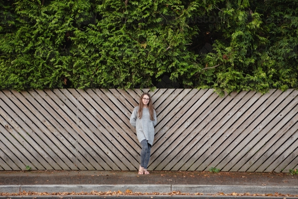 Young teenage girl in front of timber fence with green hedge - Australian Stock Image