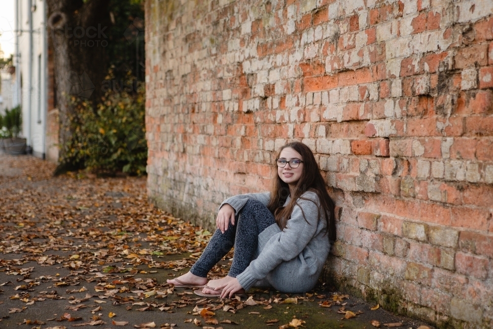 Young teenage girl leaning against red brick wall - Australian Stock Image
